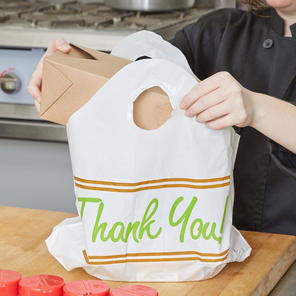 Server putting brown paper box in plastic bag for food carryout.