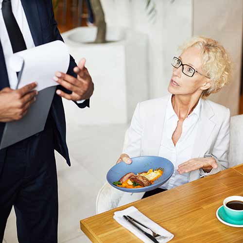 woman sitting at a table during lunch and complaining about the food to the owner of the restaurant