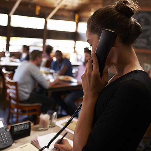 Young woman taking a reservation by phone at a restaurant.