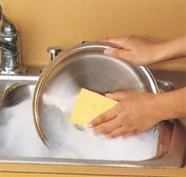 Hand scrubbing stainless steel pan with a yellow sponge in a sink full of soapy water