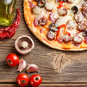 California pizza on wooden table with tomatoes, garlic, mushroom, and pepper next to it 