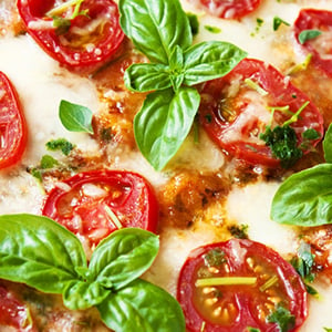 close-up view of slice of Neapolitan pizza with cheese, sliced tomatoes, and basil