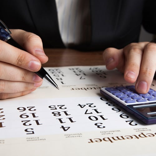 hands holding pen and typing in calculator