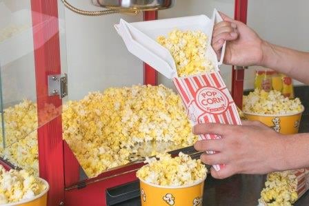 Person scooping popcorn from a popcorn machine into a paper popcorn bag