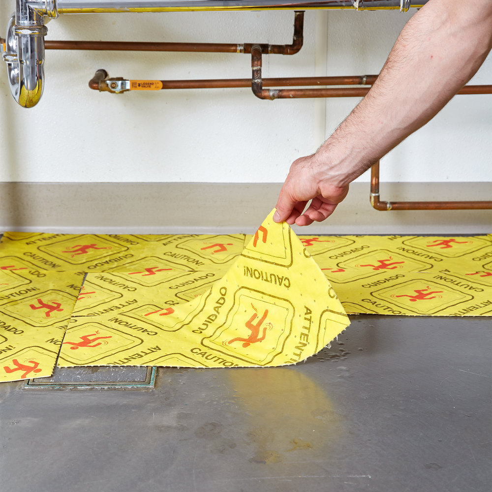Yellow spill absorbent pad being placed over a puddle of water under a sink
