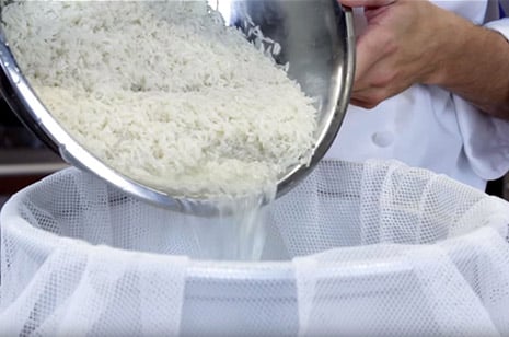 white rice being poured into a rice cooker with a rice napkin