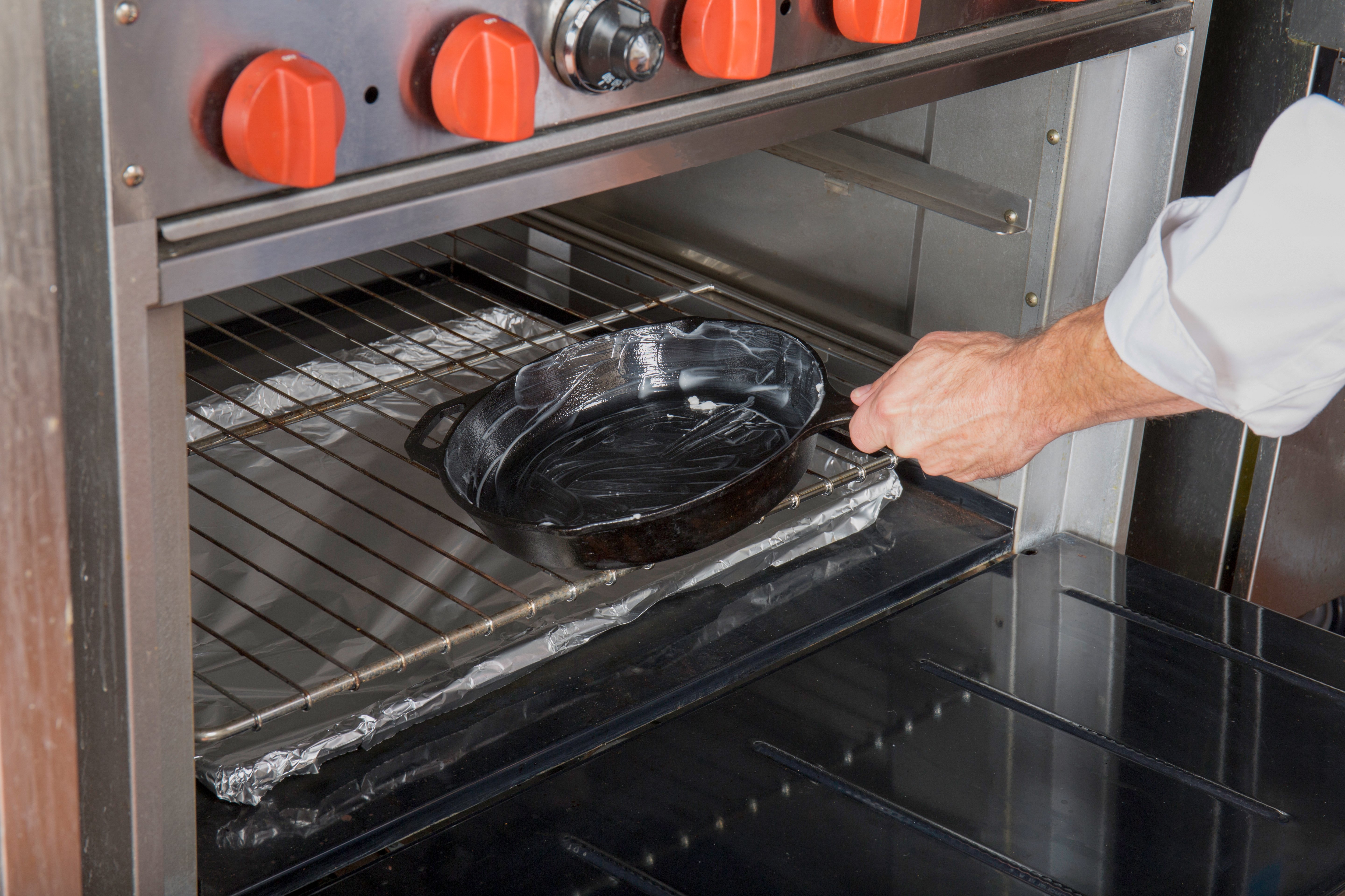 Chef placing a seasoned cast iron pan into a preheated oven