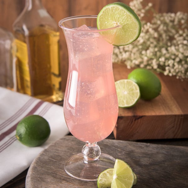 Pink cocktail and a lime wedge in a plastic hurricane glass