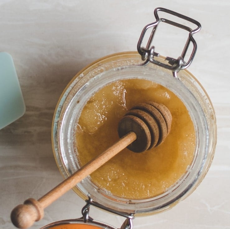 Wooden honey dipper in a glass jar of crystallized honey