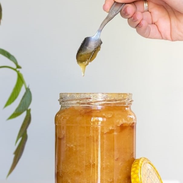 Woman holding a dripping spoonful of honey over a jar of raw honey