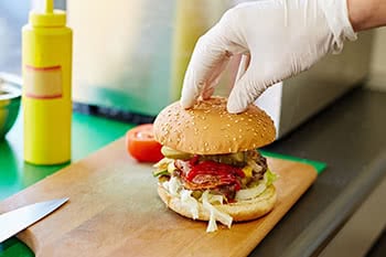a gloved hand placing the top bun on a burger