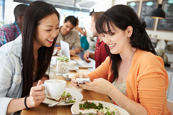 two females sitting across from each other at a cafe looking at a phone