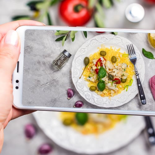 Teléfono tomando foto del plato brillante de comida a continuación