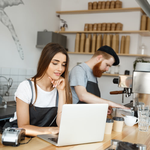 A restaurant owner behind the counter on laptop setting business goals with employee working next to her