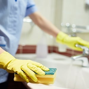 housekeeper with yellow gloves cleaning sink
