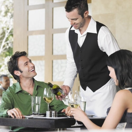 Fancy male server pouring wine to male who sits across from female