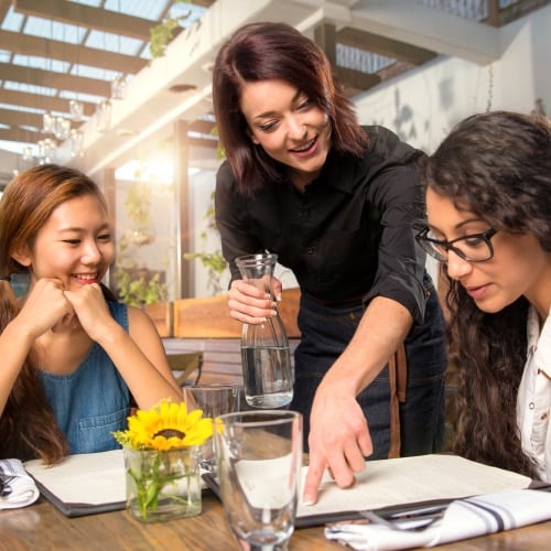 Female server pointing at menu at table of two female guests