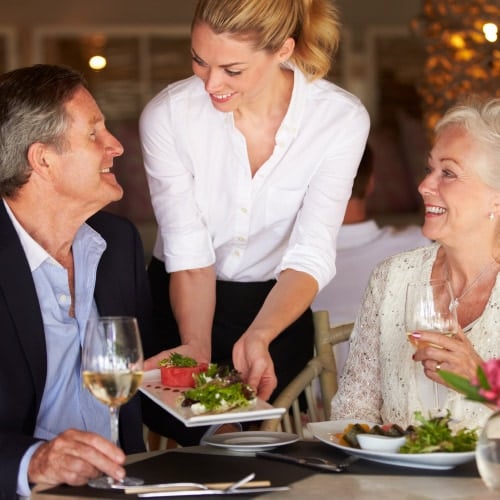 Female server dropping of plate of food to table of older man and woman