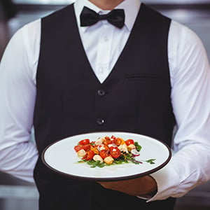 waiter in a black outfit holding a white plate with veggies