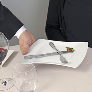 waiter in a black coat removing a white plate from a table